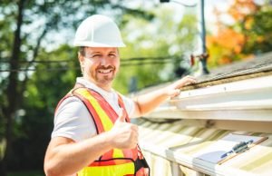 A man with hard hat standing on steps inspecting roof